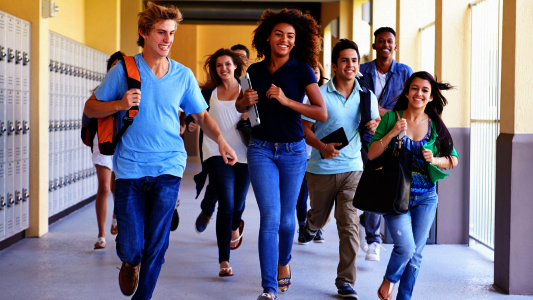 Schülerinnen und Schüler rennen fröhlich über einen Schulflur